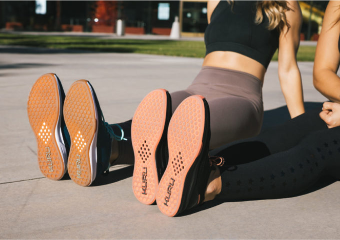 Two people sitting with their feet out wearing KURU shoes