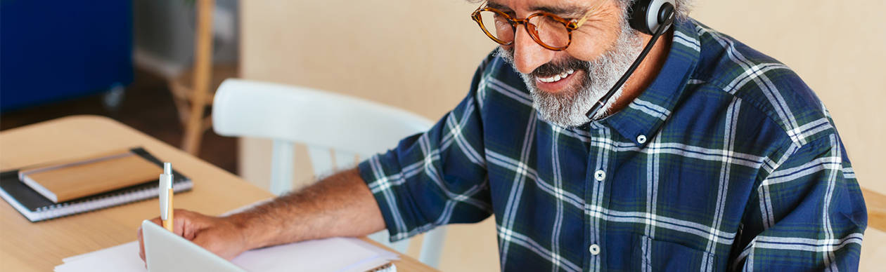 Smiling older man wearing a phone headset and looking at a laptop
