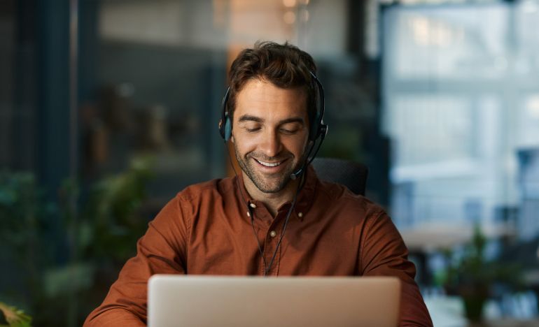 Man in a red shirt and phone headset smiling and looking at a laptop
