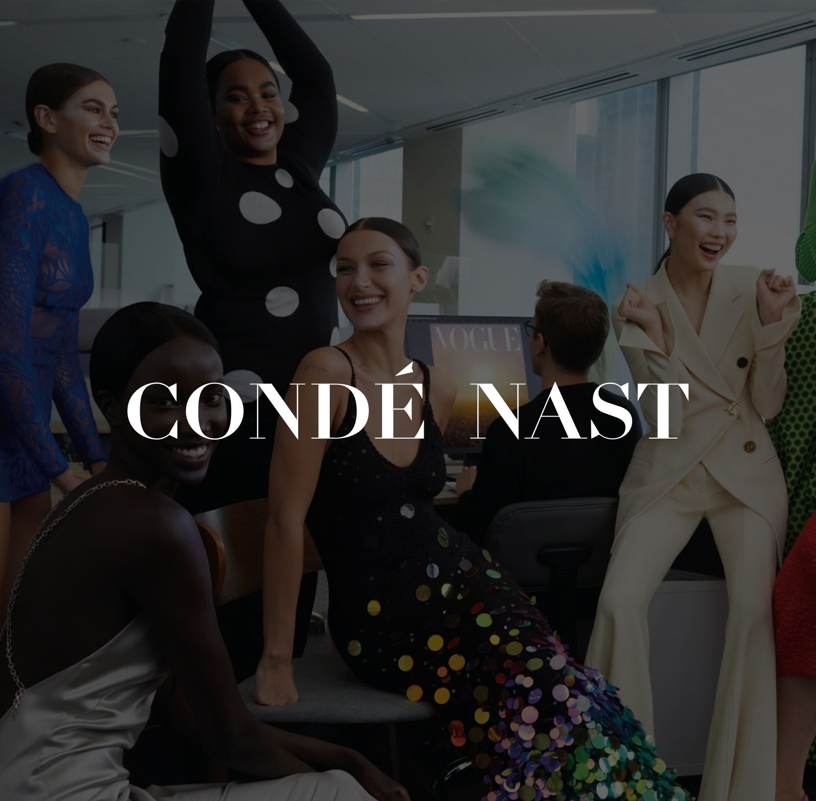 A diverse group of people joyfully celebrate in a modern office, with some sitting and others standing. They're dressed in colorful, stylish attire.