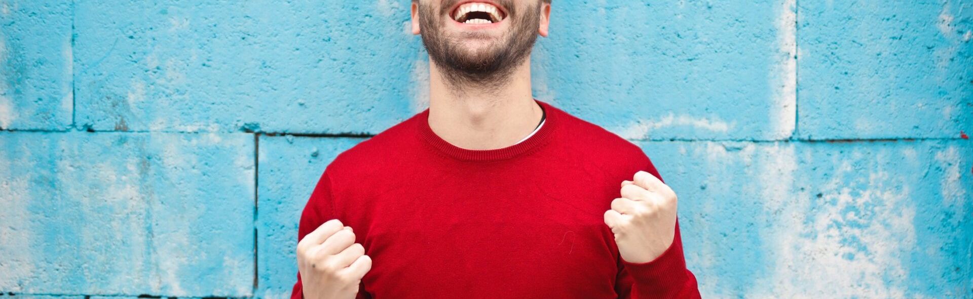 Happy man celebrating in front of a blue wall