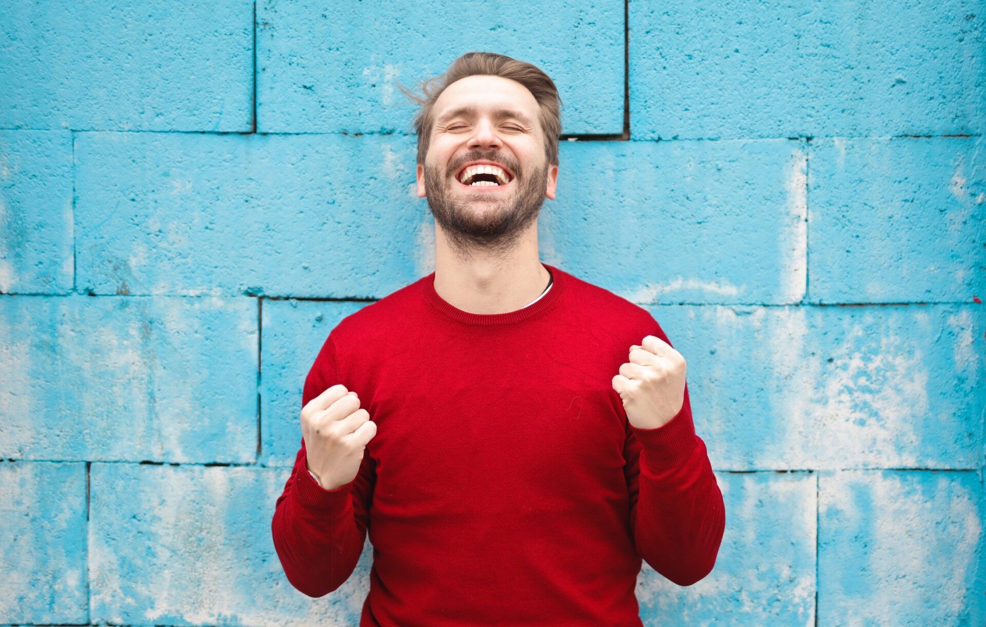 Happy man celebrating in front of a blue wall