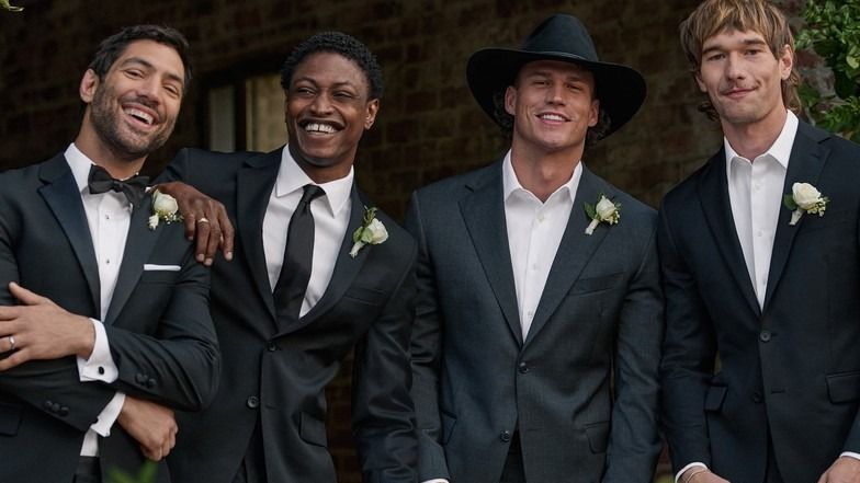 Four groomsmen in suits laughing together at a wedding