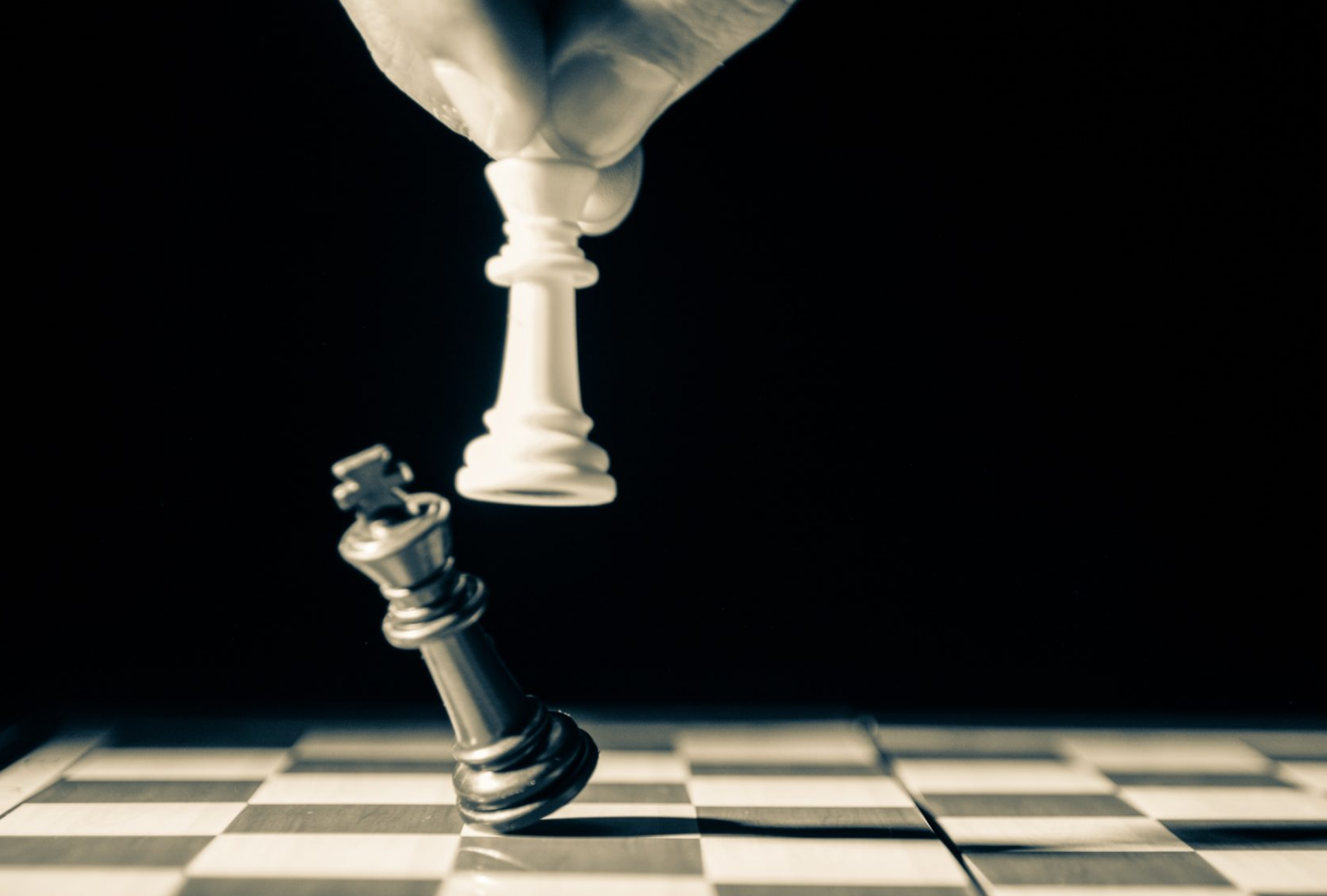 Image of a hand holding a chess piece knocking over another chess piece