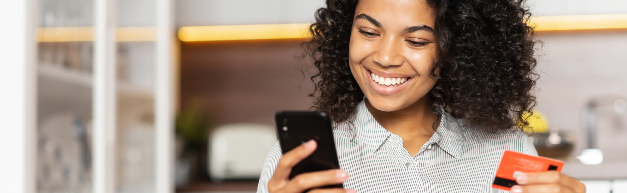 Woman smiling at her smartphone holding a credit card