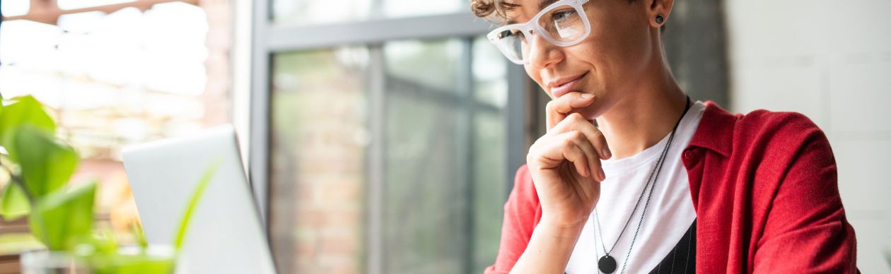 Bespectacled woman looking ponderously at her laptop