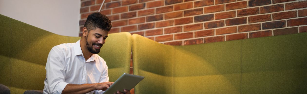 Man sitting and smiling down at a tablet he's typing on