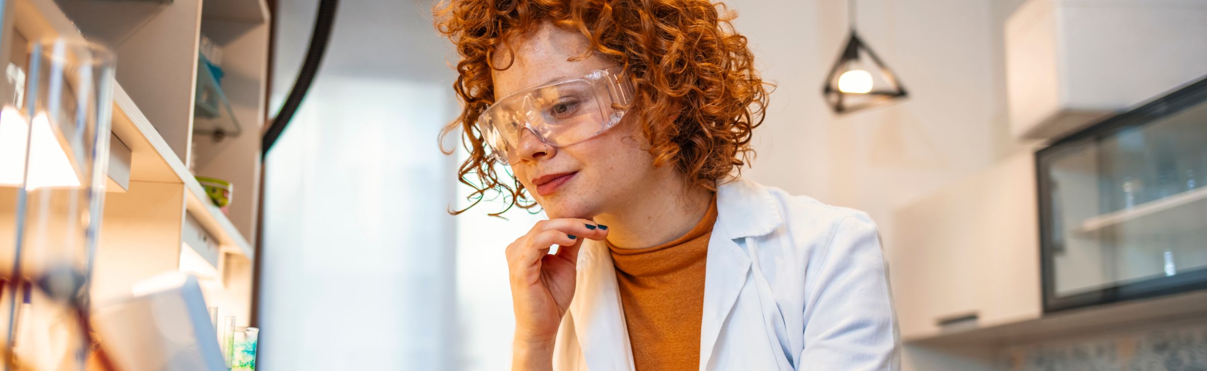 Scientist wearing safety goggles in a lab reviewing laptop