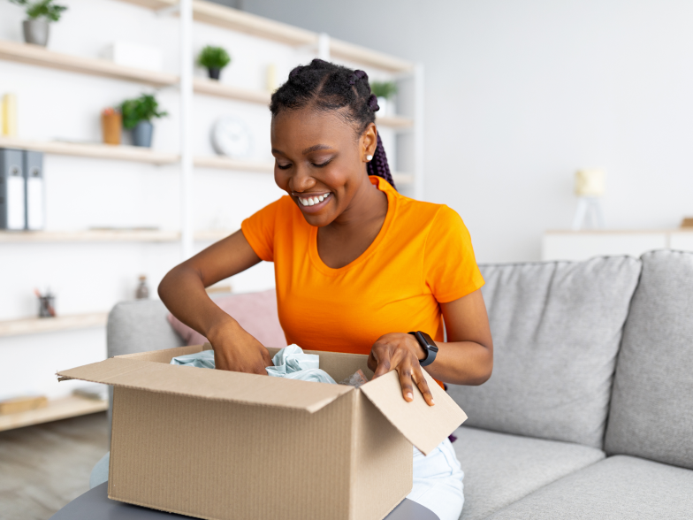Smiling woman unpacking an online order from a cardboard box in her living room