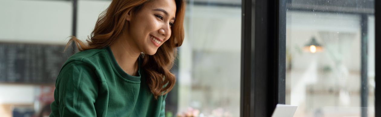 Woman in a green sweatshirt smiling at her laptop