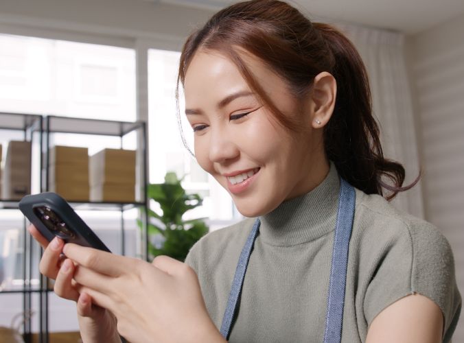 Store clerk in apron looking at phone interacting with a chatbot