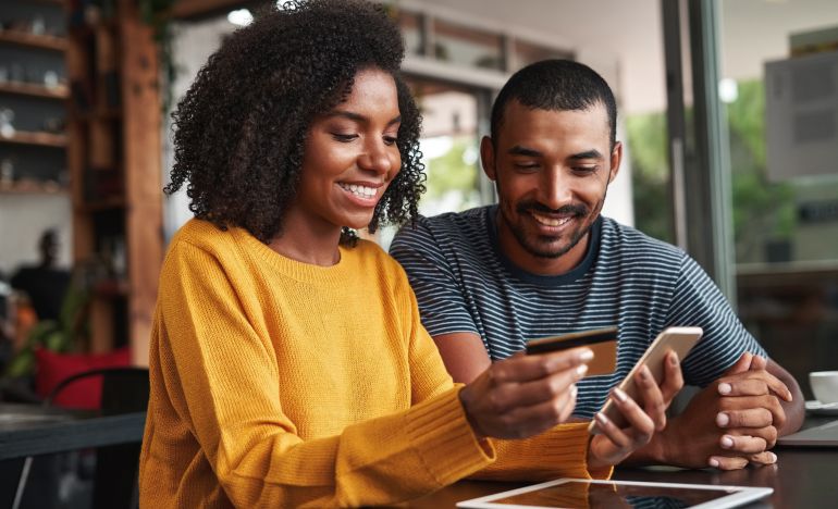 Two people looking at a tablet, one of which is preparing to buy something on her smartphone
