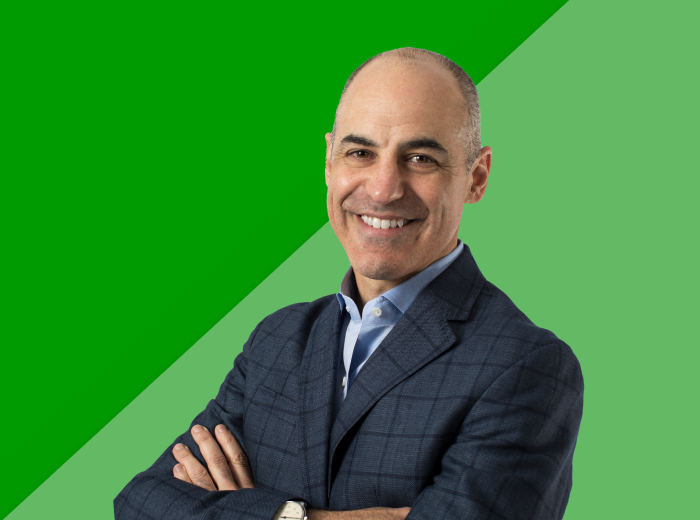 Smiling man in a plaid suit with arms crossed, on a split green background. The tone is professional and approachable.