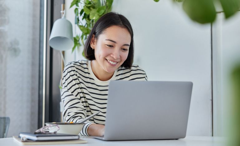 Woman in a striped shirt smiling at her laptop