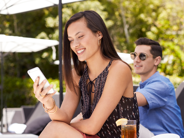 Smiling woman seated outdoors looking at her smartphone