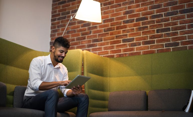 Man sitting and smiling down at a tablet he's typing on