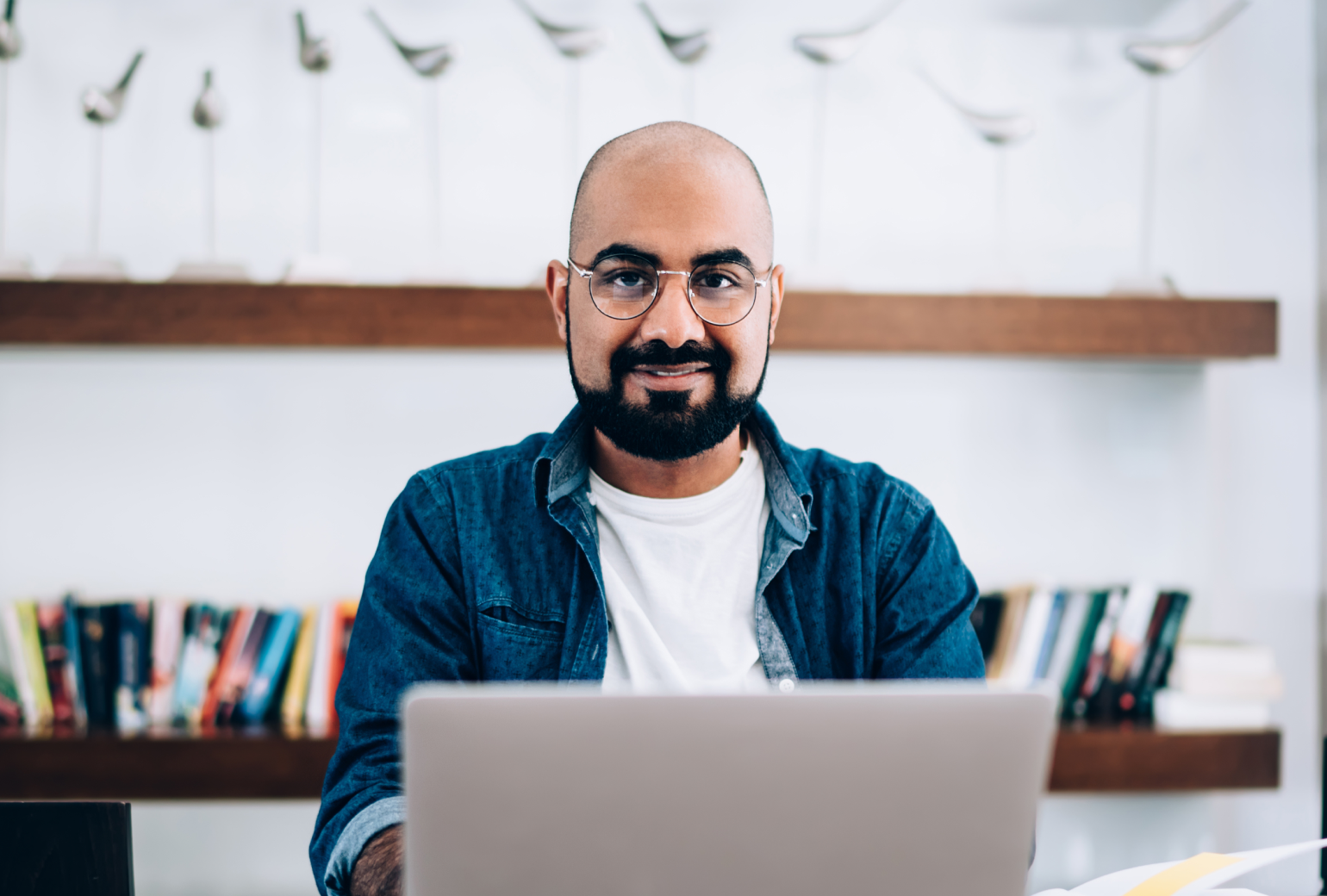 Man in glasses sitting in front of a laptop smiling at the camera