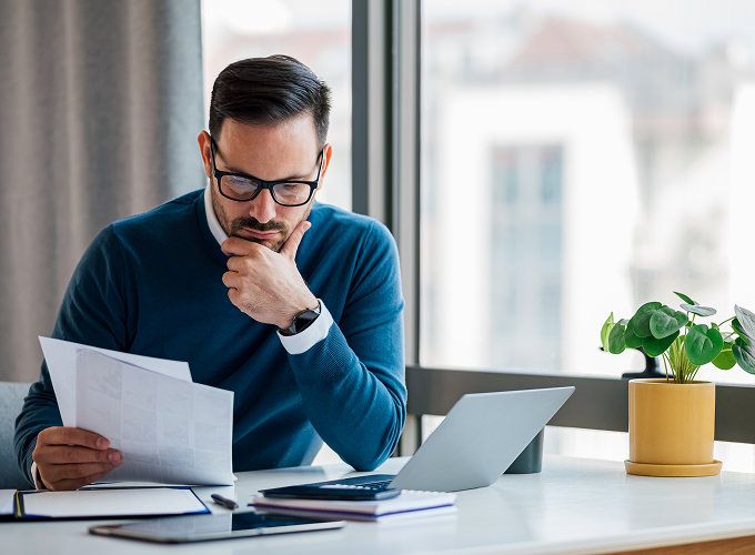 Man reviewing paperwork while sitting with laptop