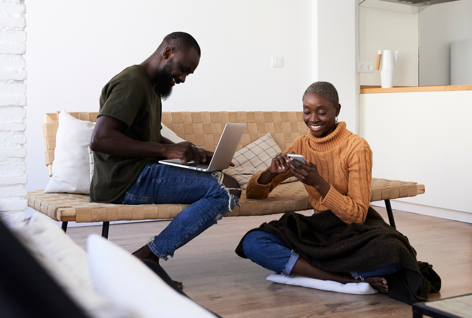 Two people sitting in a living room, a man with a laptop and a woman with a smartphone