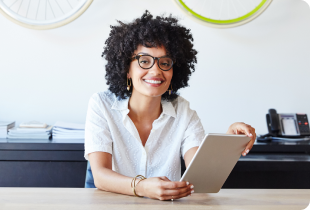 Woman in glasses and a white shirt holding a tablet and smiling in front of a decorative hanging bicycle