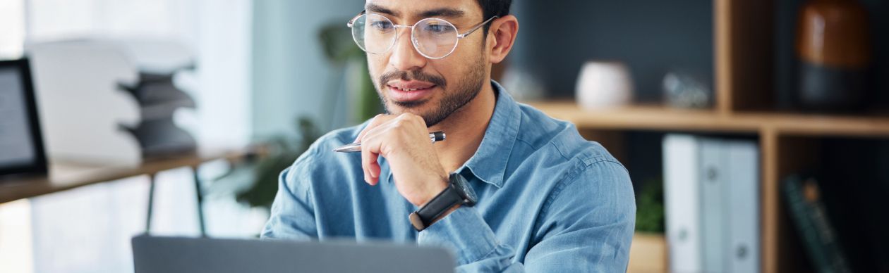 Bespectacled man looking seriously at his laptop