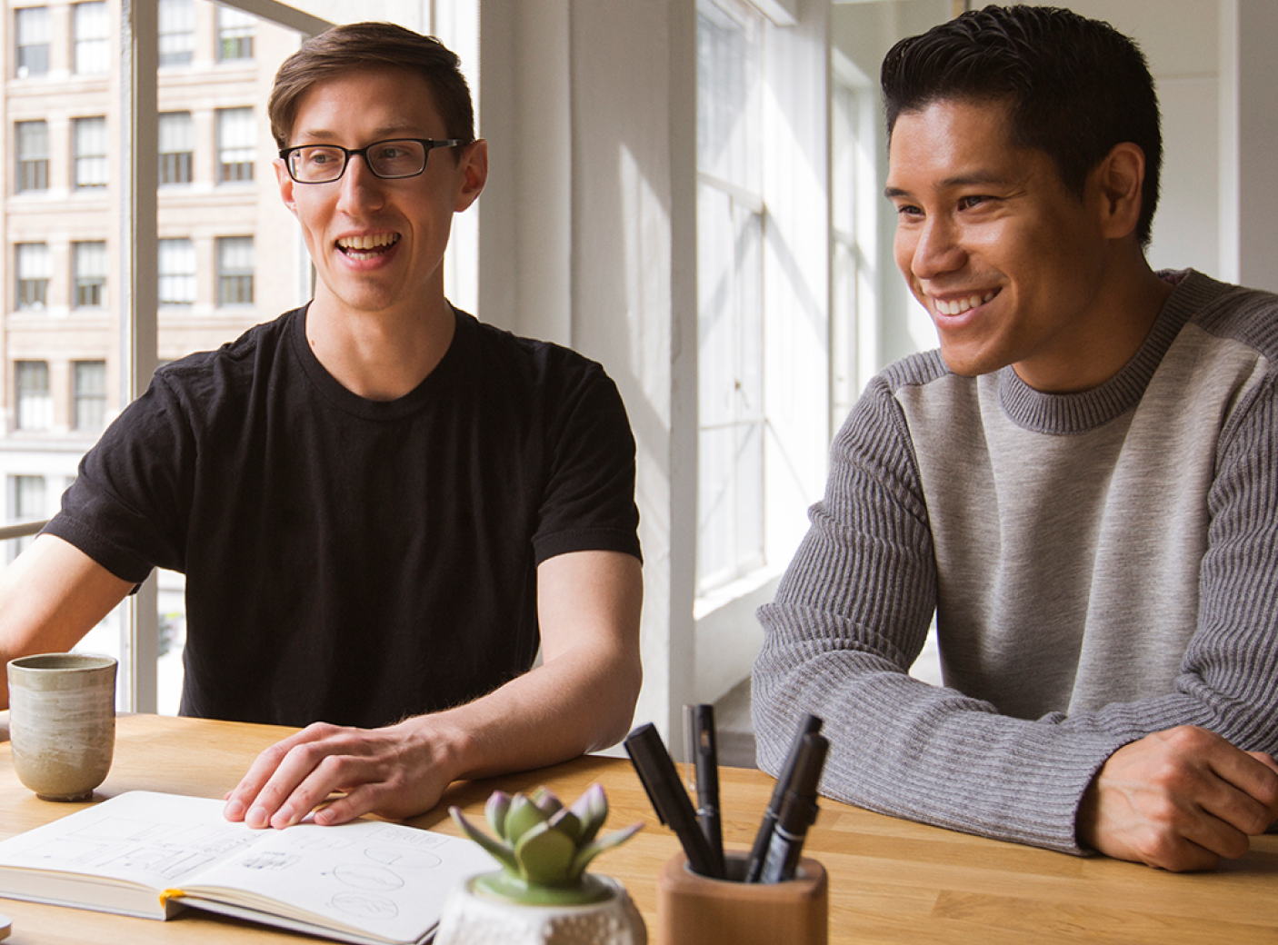 Two men sitting at a desk with an open notebook