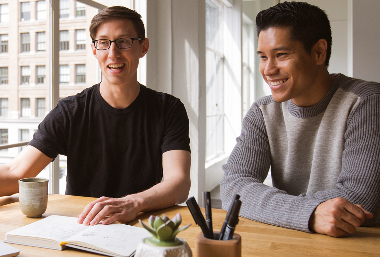 Two men sitting at a desk with an open notebook