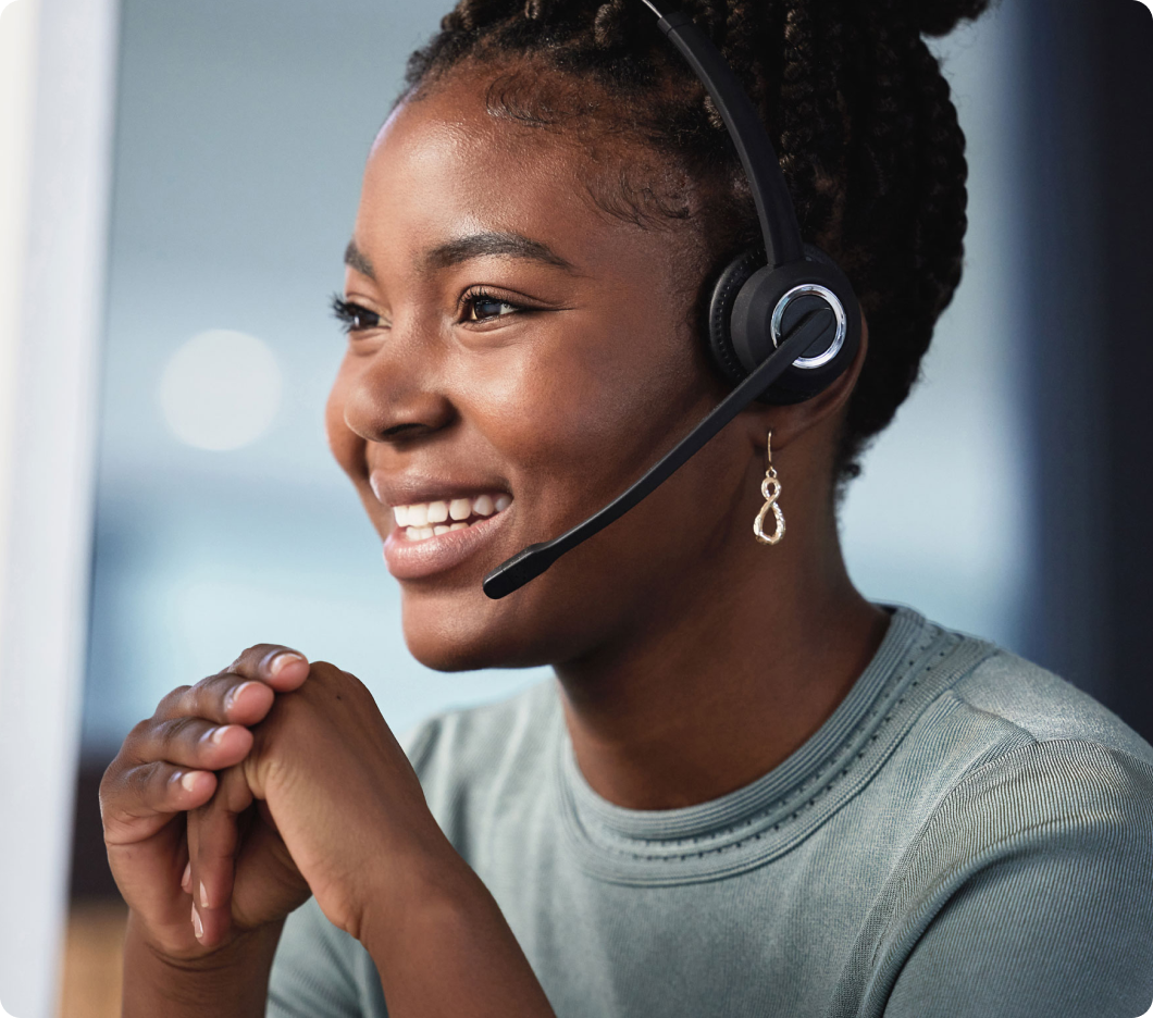 A smiling woman wearing a headset and patterned earrings sits with hands clasped, conveying a friendly and professional tone.