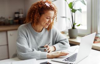 A woman browsing on her laptop and holding a coffee cup