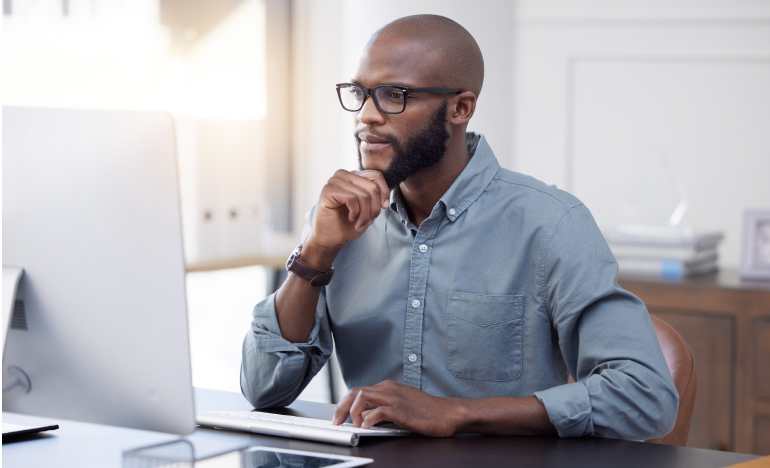 Bespectacled man looking ponderously at a laptop