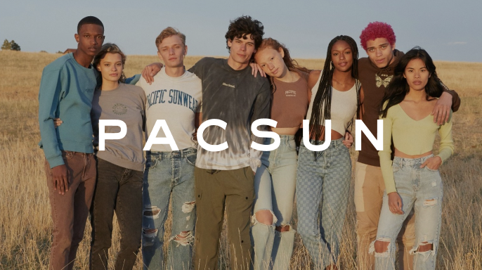 A diverse group of eight people stand closely in a sunlit field, wearing casual PacSun clothing. They appear relaxed and content, embodying a youthful vibe.