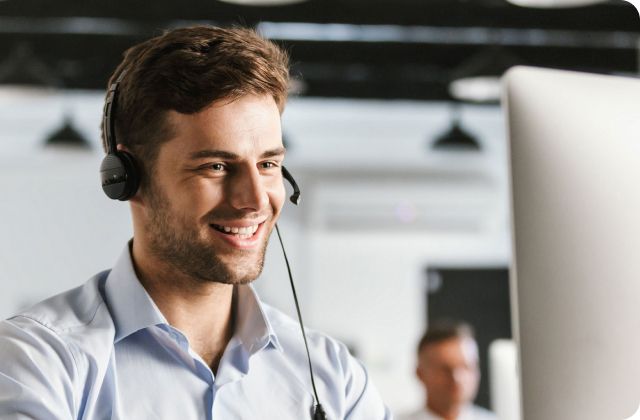 Man smiling with a phone headset and looking at a computer monitor