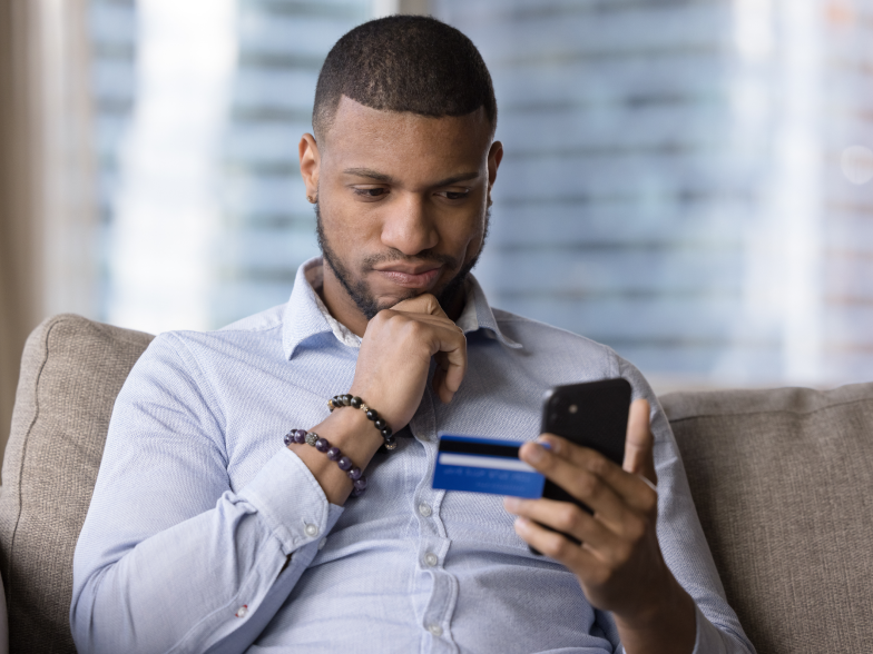 Man on the couch, hand on chin, card in one hand and phone in the other