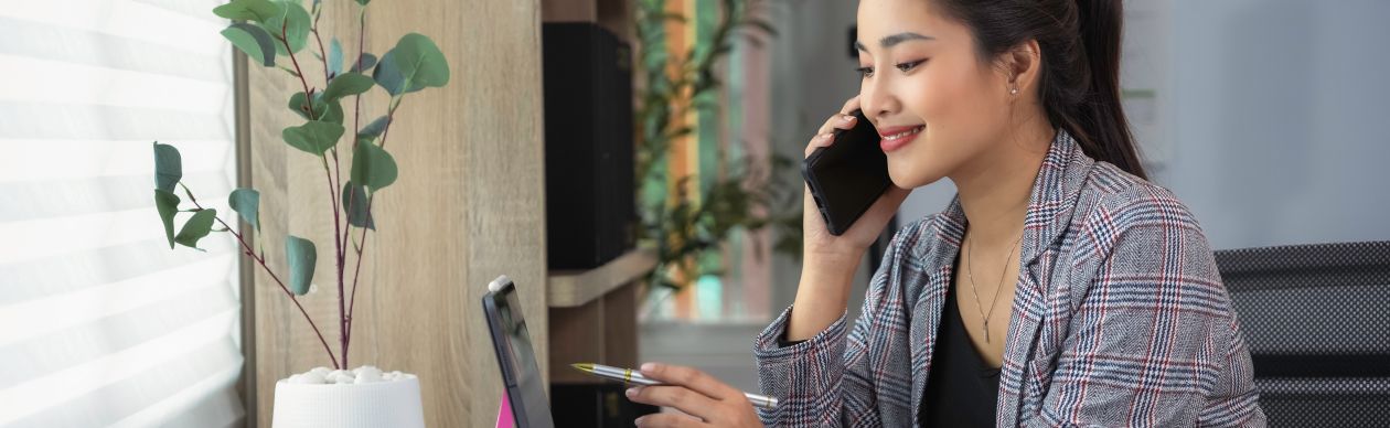 A smiling professional woman on her smartphone and looking at a computer monitor