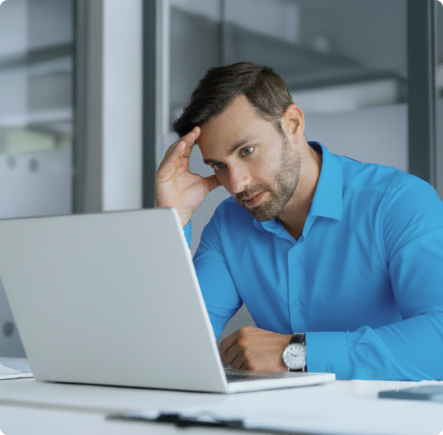 A man in a blue shirt looks at a laptop with a concerned expression, resting his head on one hand. The office setting is modern and minimalistic.
