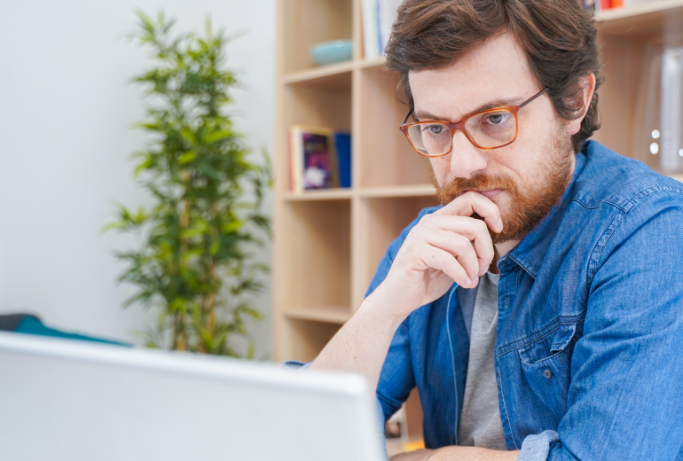 Bespectacled man looking seriously at a laptop