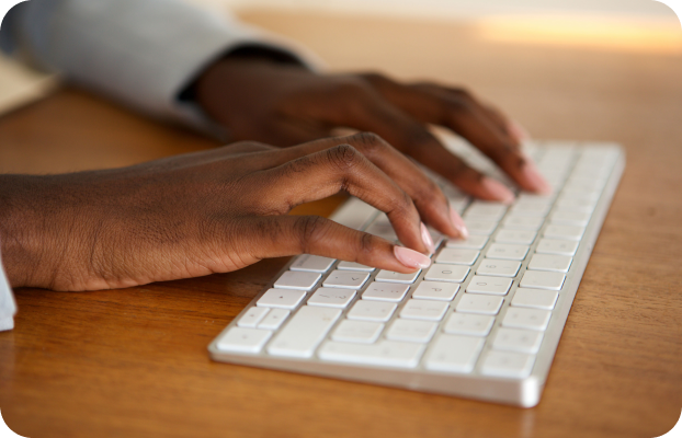 Hands typing on a white keyboard placed on a wooden desk, conveying a sense of productivity and focus. The lighting is warm and inviting.
