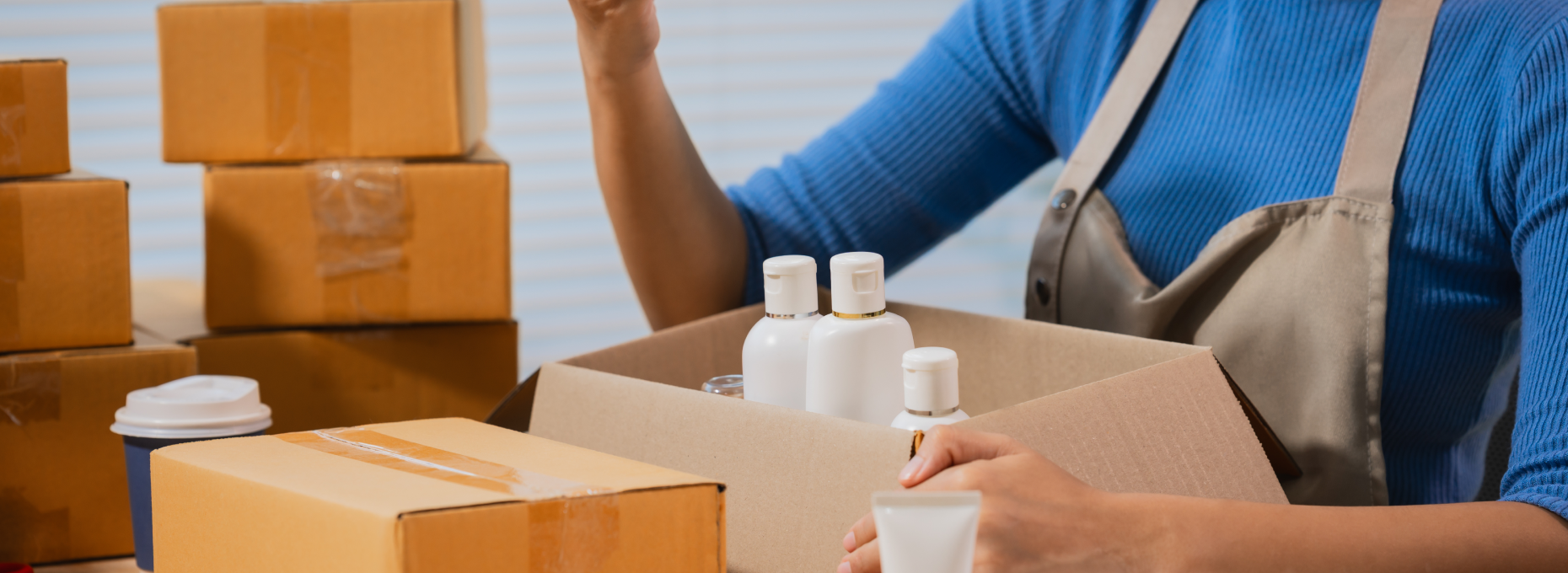 Small business owner packing a set of matching skincare bottles into a shipping box at her desk