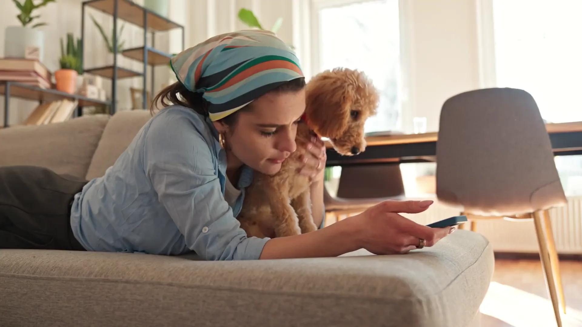 Customer relaxing on her couch with her puppy while checking her phone