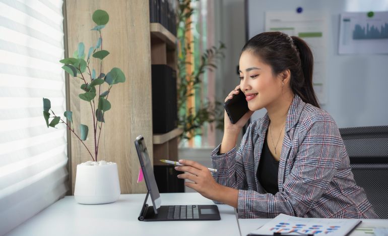 A smiling professional woman on her smartphone and looking at a computer monitor