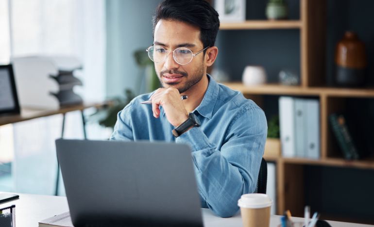 Bespectacled man looking seriously at his laptop