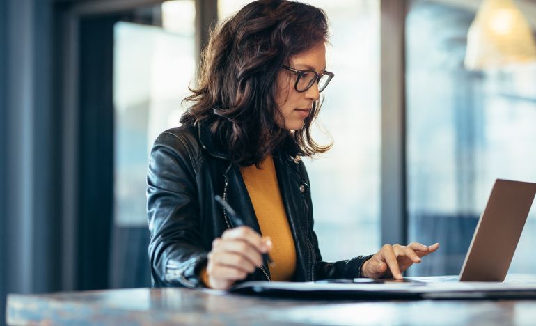 A bespectacled businesswoman looking at a laptop