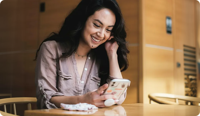 Woman smiling at phone in a cafe, engaged in a chat about exchanging a jacket. Texts on screen express friendly customer service.