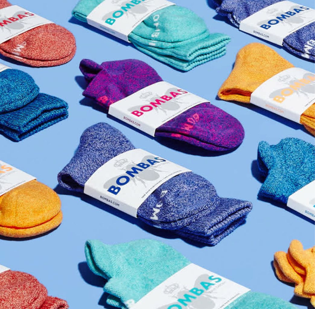 Colorful array of Bombas socks neatly arranged on a blue background, featuring vibrant hues like pink, blue, and orange, each labeled with branding. Vibrant and cheerful.