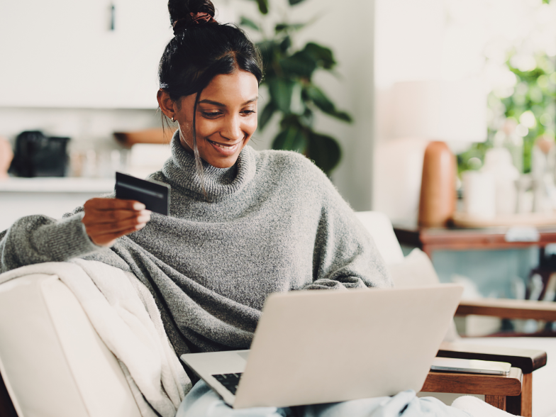 Woman sitting on a couch, smiling while looking at her laptop and holding a credit card.
