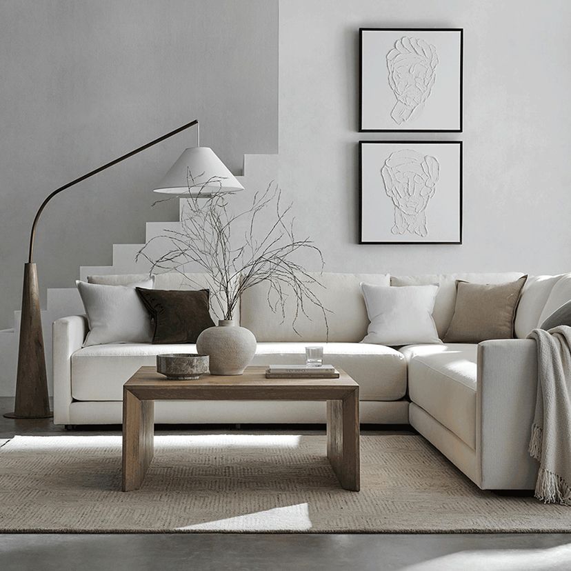 A modern living room with a white sectional sofa, neutral cushions, and a wooden coffee table. Abstract art and a minimalist lamp create a calm, stylish atmosphere.