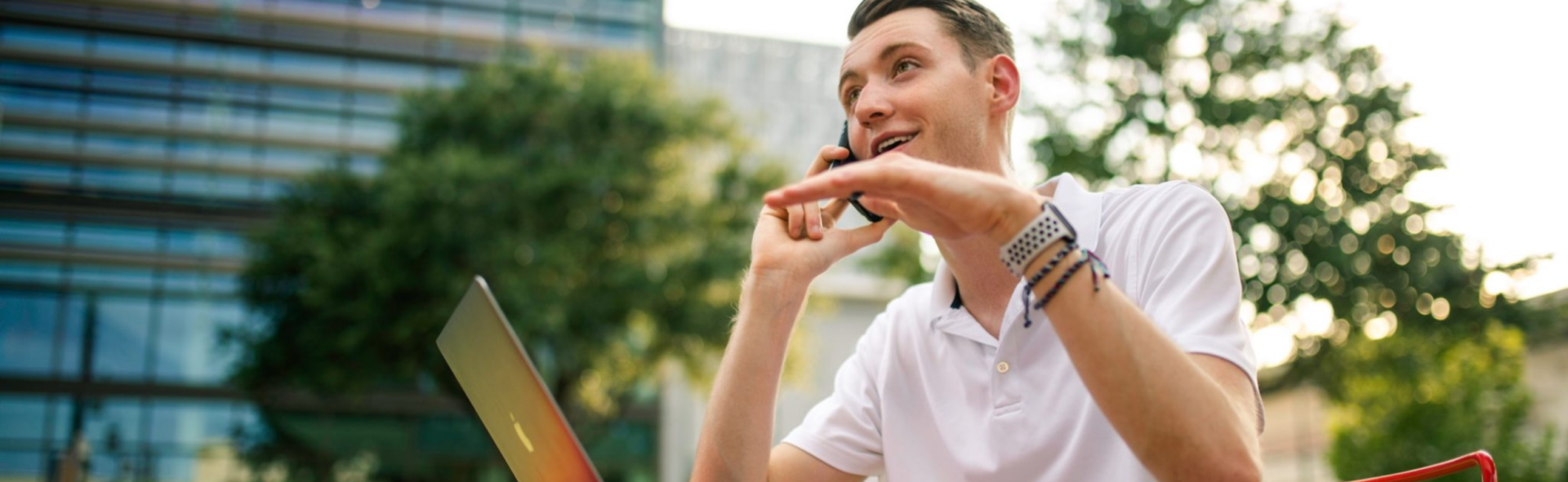 Man in a polo shirt talking on his cell phone in front of a laptop