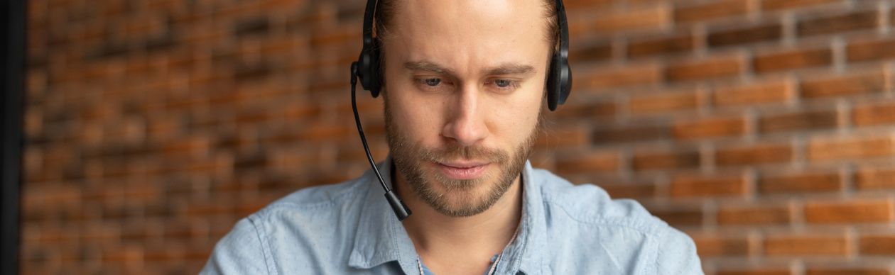 Bearded man with a phone headset looking at a laptop