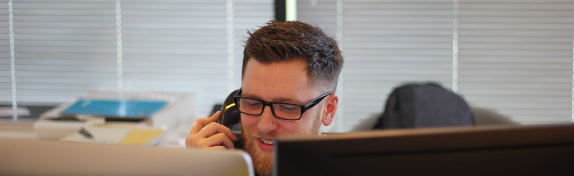 Man in glasses on the phone in front of two monitors