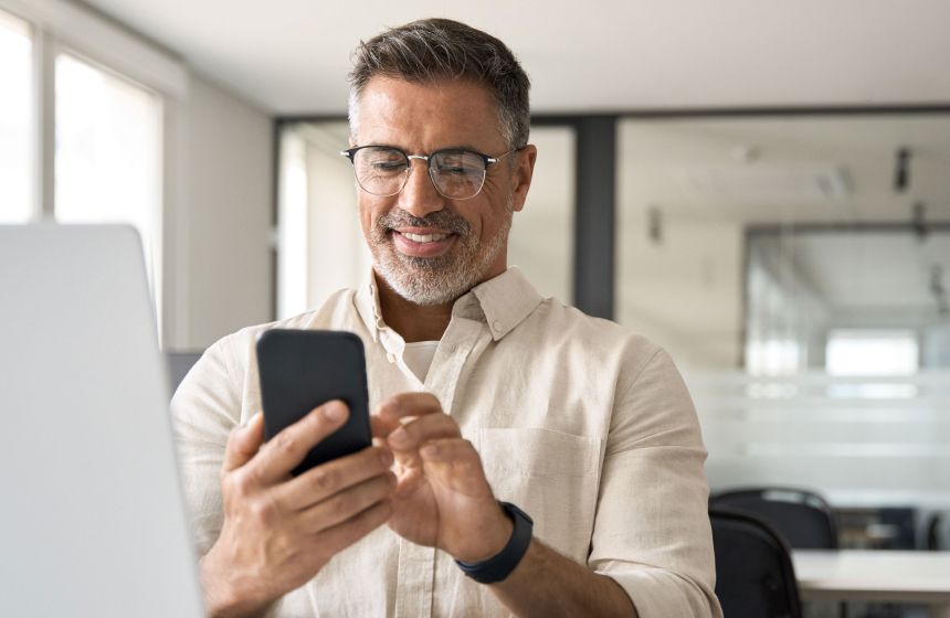 Man sitting at his computer desk, playing on his phone